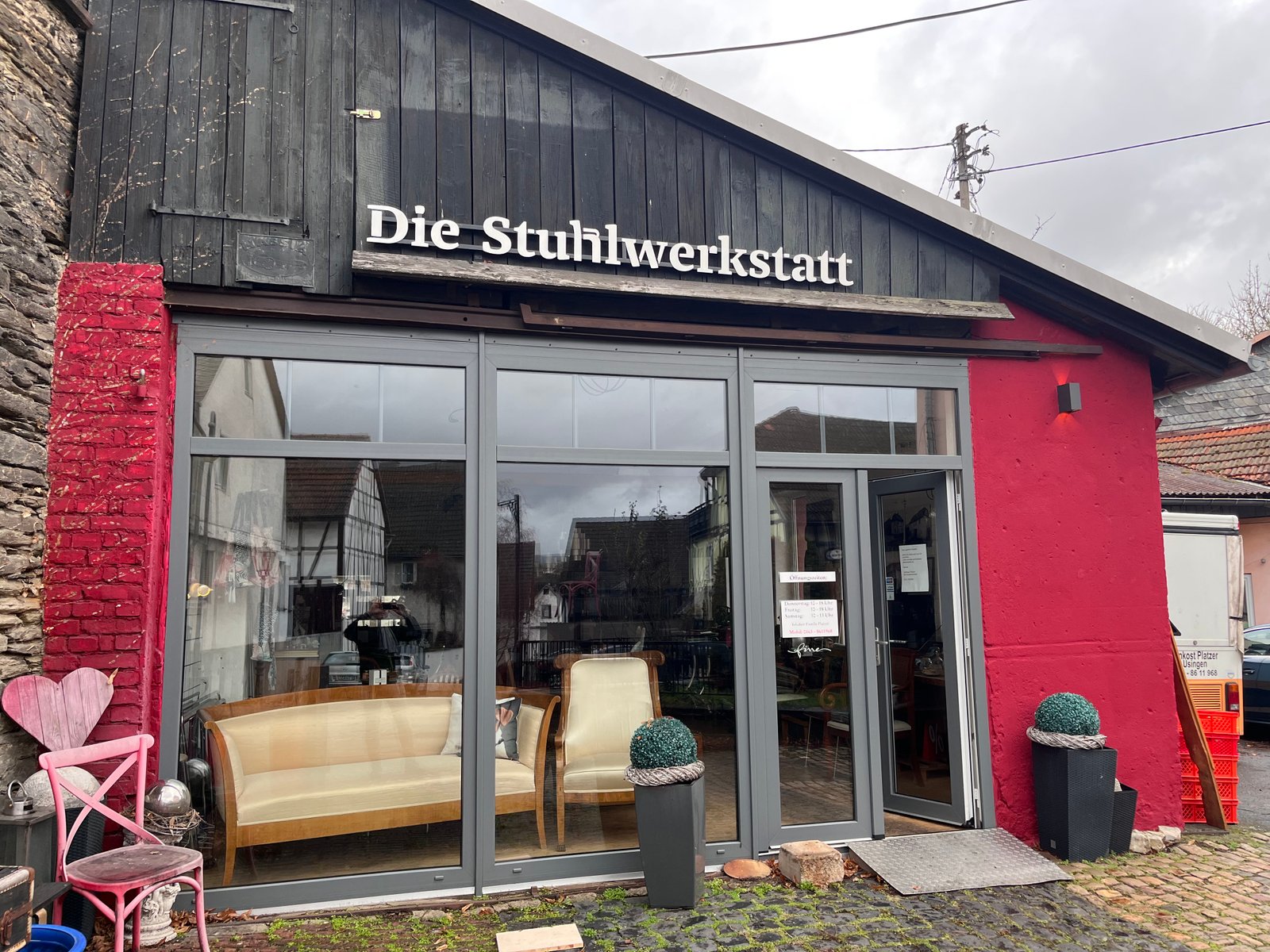 Außenansicht der Stuhlwerkstatt mit roter Fassade, dunklem Holzgiebel und großem Schaufenster